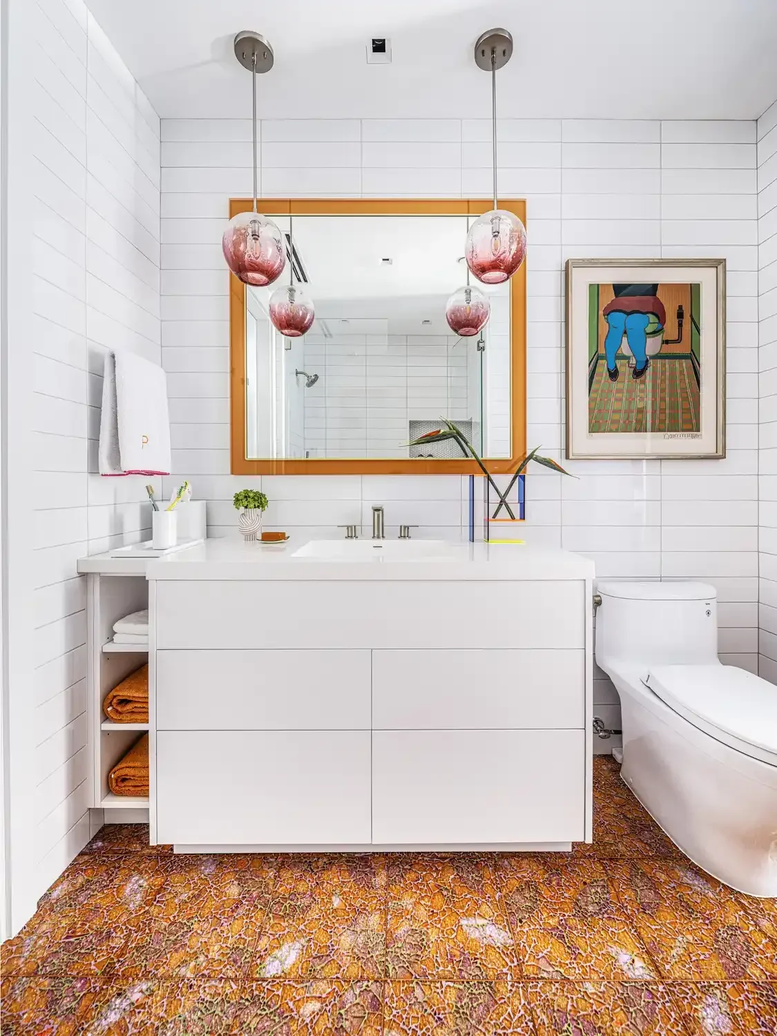 White bathroom with a rectangular mirror, pendant lights, white vanity, geometric patterned orange and brown tiled floor, and a framed artwork depicting a person with blue pants and red shirt in a colorful setting.