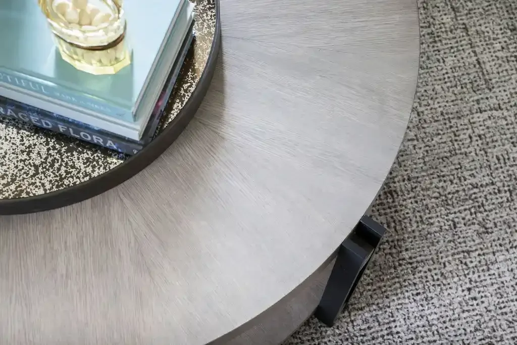 Close-up of a round wooden coffee table with a black tray holding books and a candle on a textured carpet.