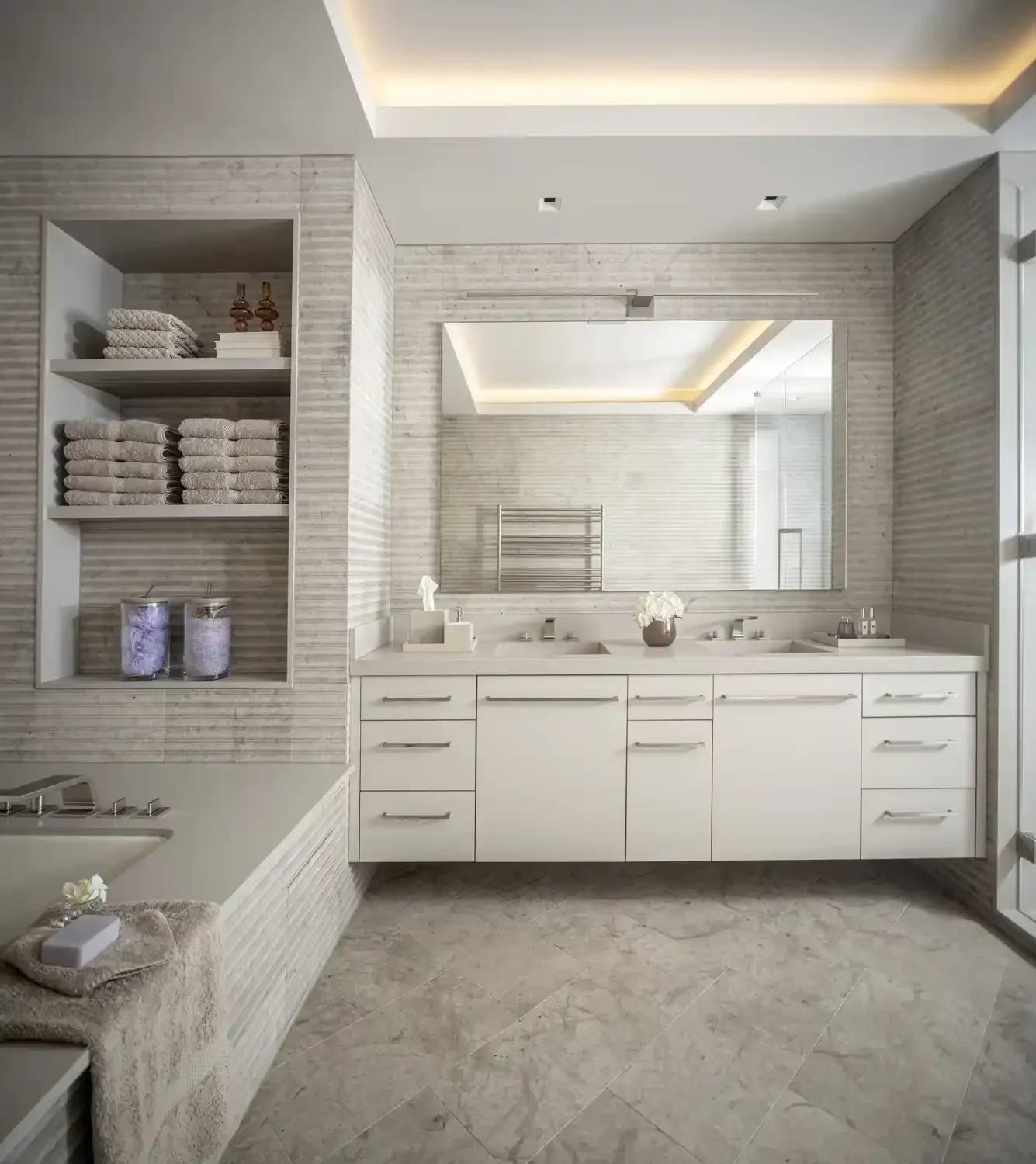 Modern bathroom with a large mirror, white double sink vanity, and open shelves with towels and decorative candles.