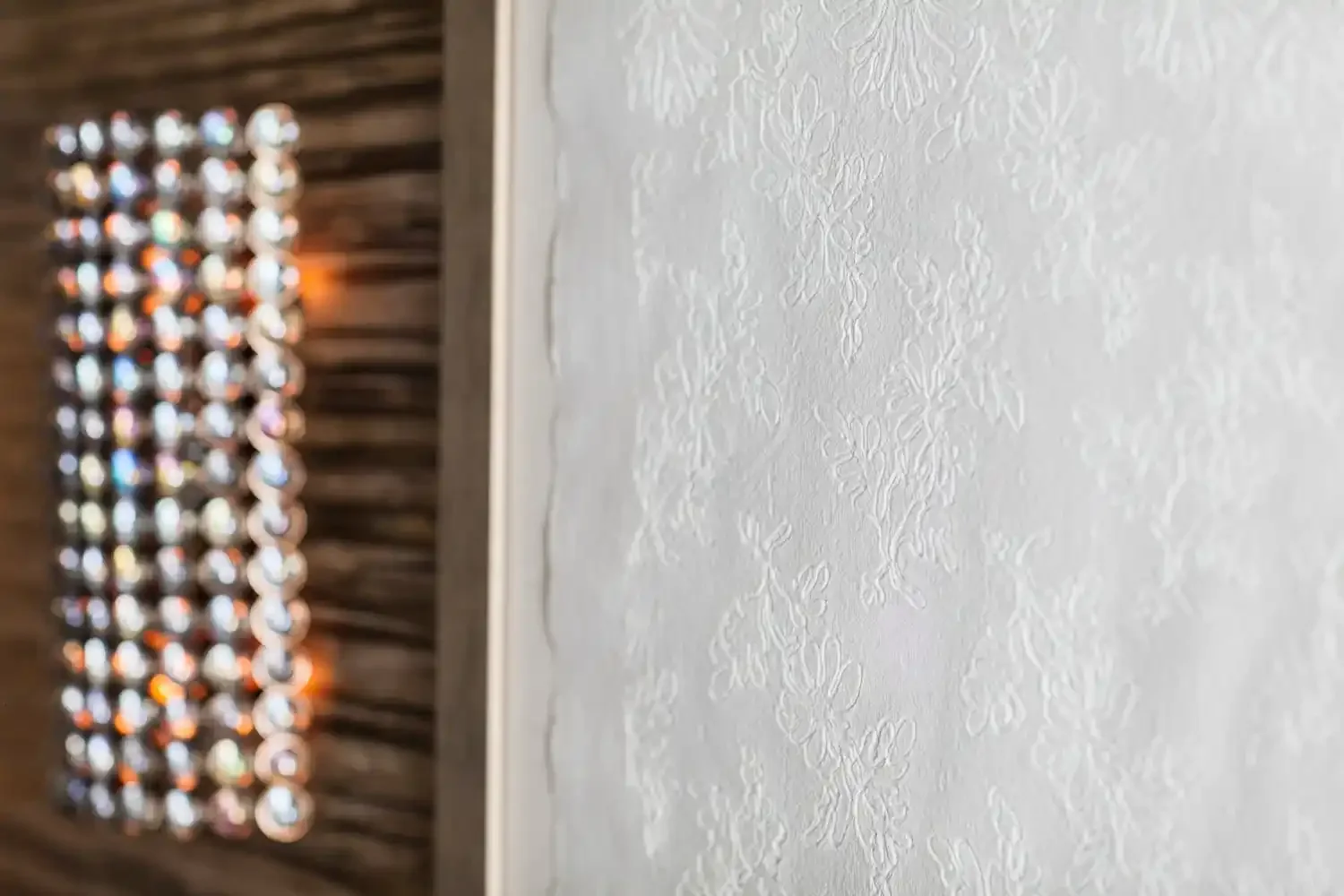 Close-up of textured white wall with decorative design, and blurred background of hanging bottles or jars on a wooden wall.