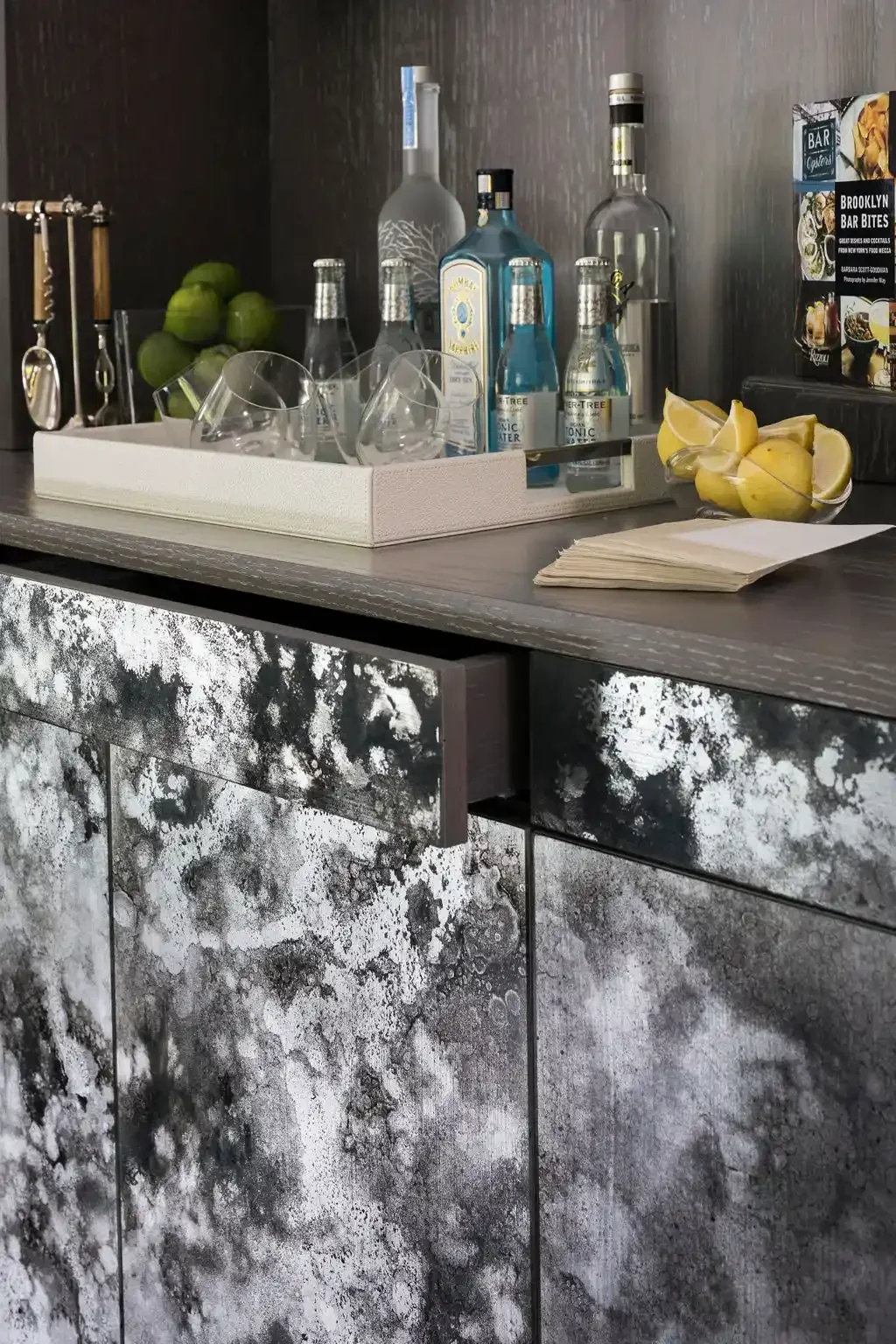 Bar counter with bottles of alcohol, lime, lemons, glasses, and cocktail ingredients in a modern setting.