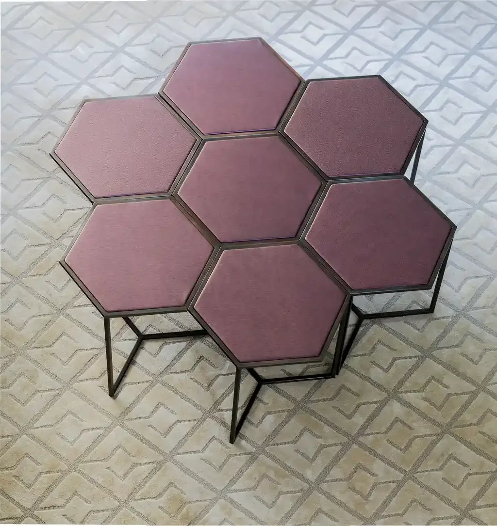 A table made of six interconnected hexagonal panels, with pink and purple cushioned surfaces and black metal frames, placed on a patterned beige and gray carpet.
