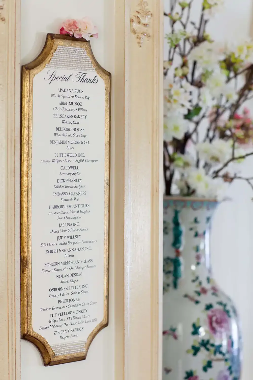 A framed list of businesses and services titled 'Special Thanks,' mounted on a wall next to a floral arrangement in a decorative vase.