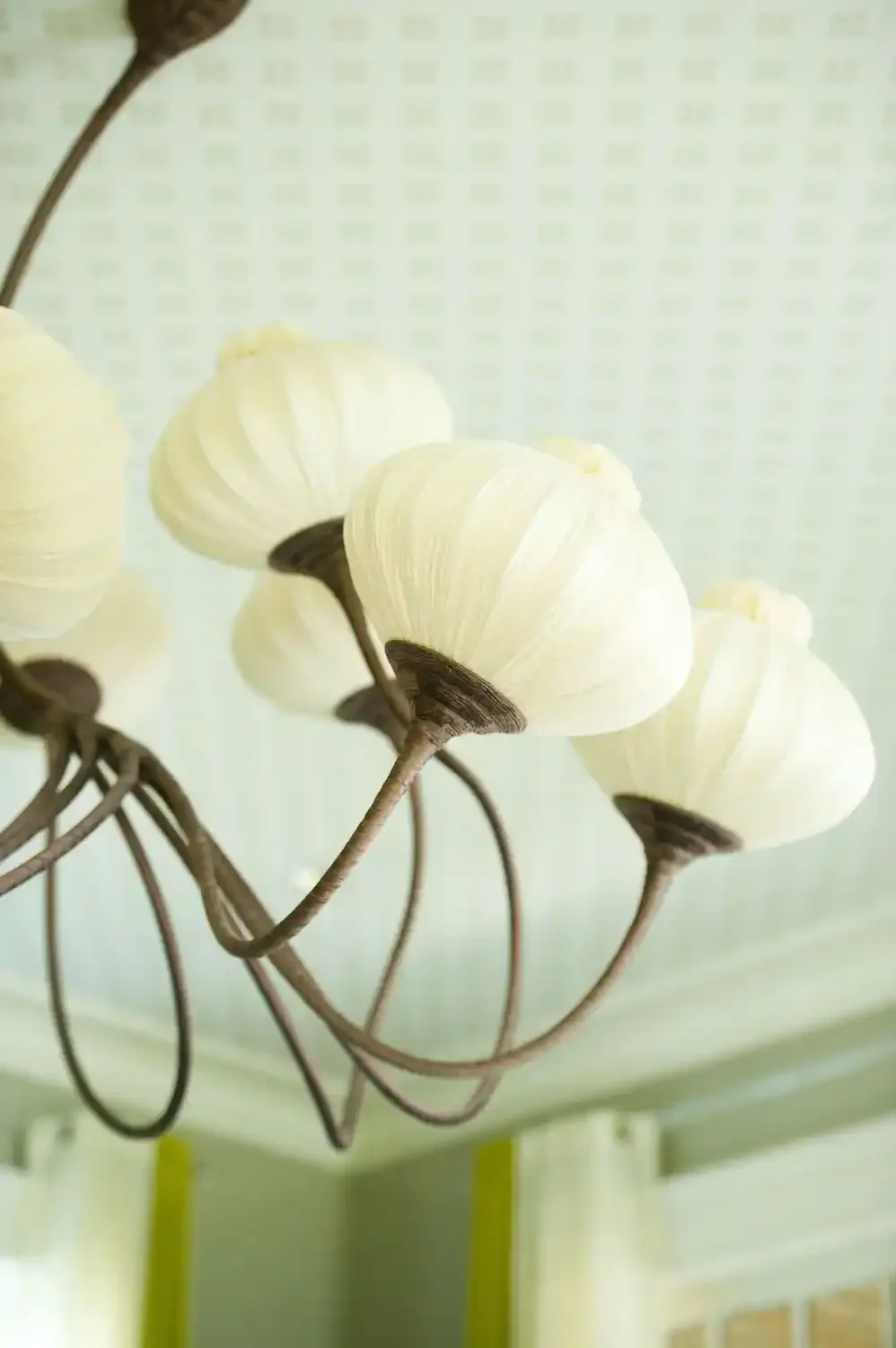 Close-up of decorative lamp with cream-colored flower-shaped lampshades and brown metal stems, mounted on a ceiling.