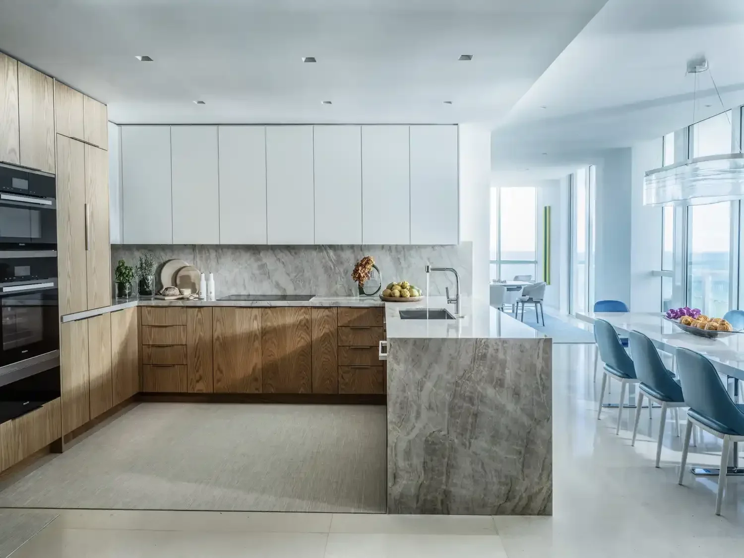 Modern kitchen with wood and white cabinets, marble countertops, and a dining area with blue chairs