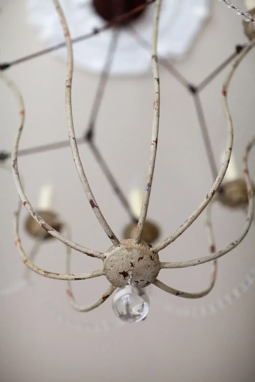 Close-up of an old, rusty ceiling light fixture with a white metal frame and a crystal ornament hanging at the bottom.
