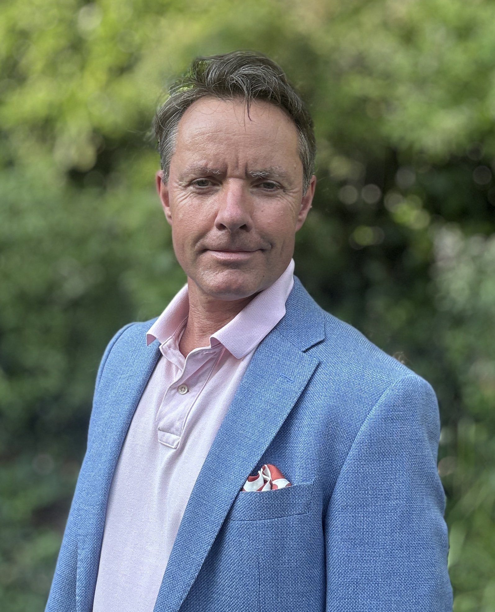 William Franklin: Founder Reset & Perform wearing a blue sports jacket, pink polo-shirt and smiling in a relaxed way