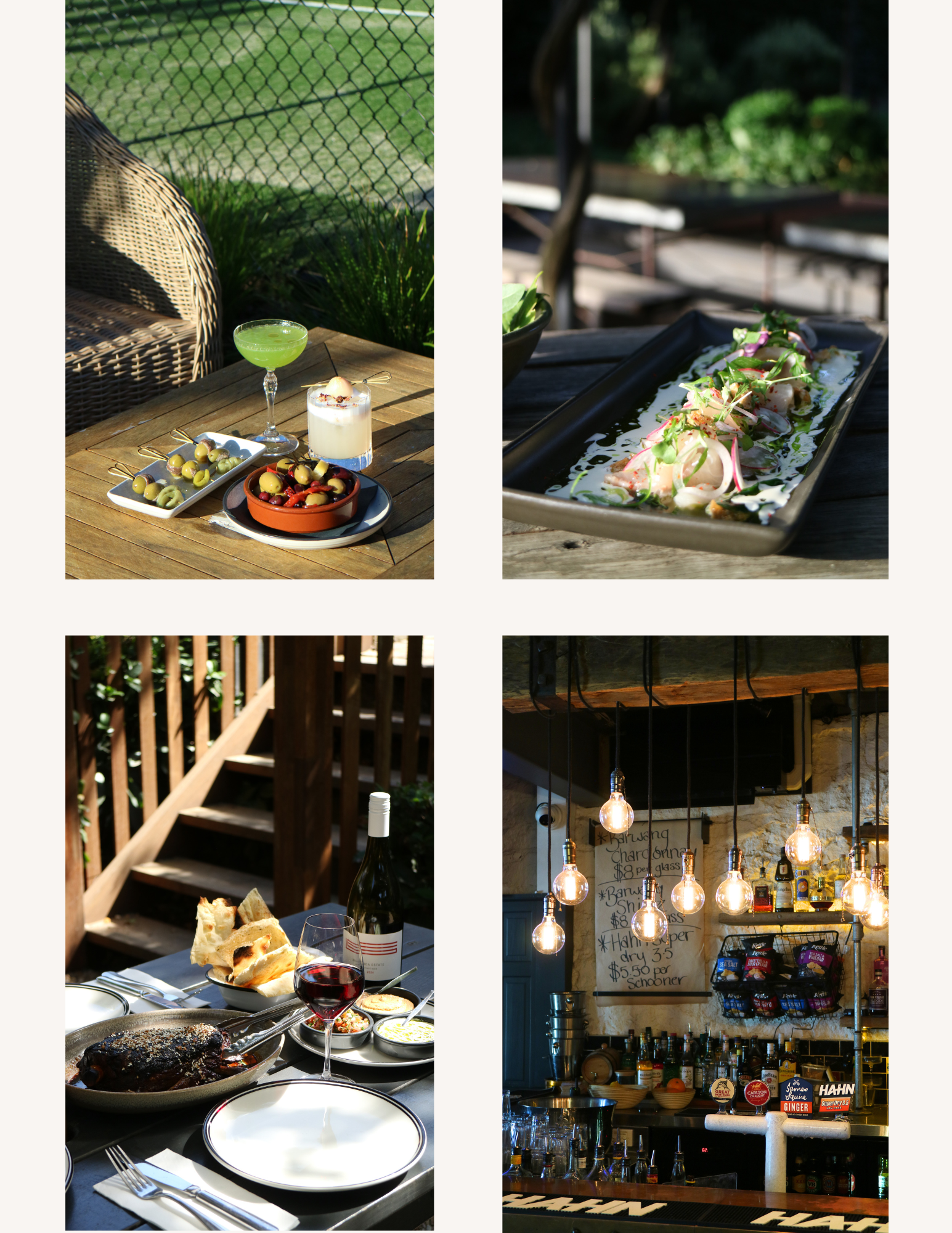 Outdoor dining scene showing a wooden table with plates of food, salad, and drinks, with a bar area behind it featuring hanging lights and a menu board.