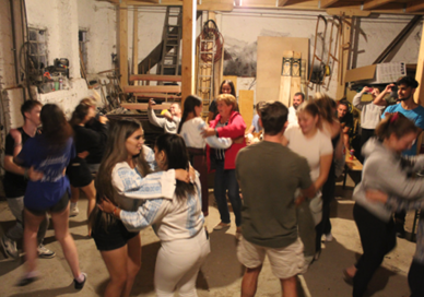 Group of people dancing and socializing in a garage or basement space.