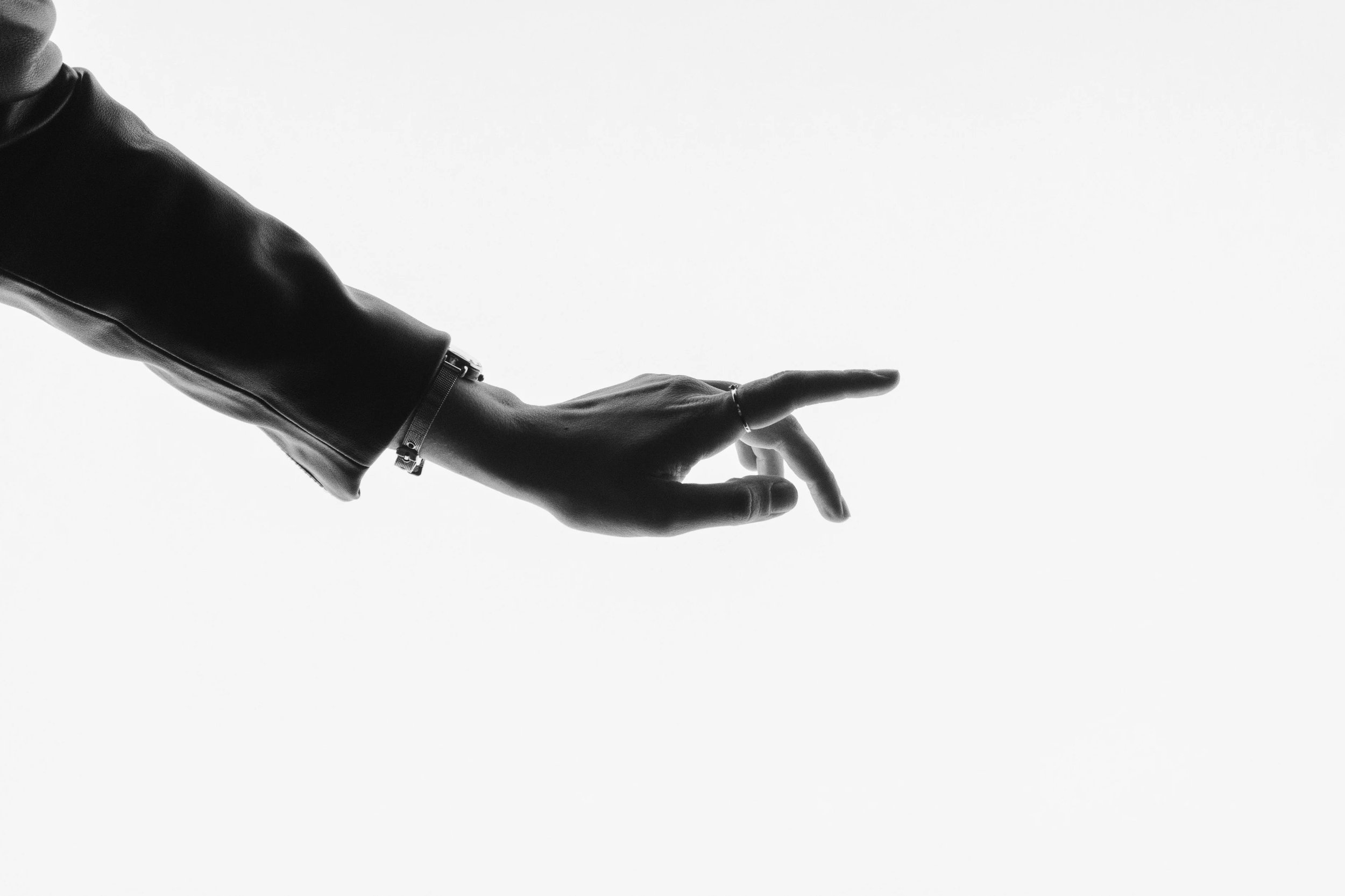 Black and white close-up of a person's hand with a bracelet, extending horizontally with fingers slightly apart, against a plain background.