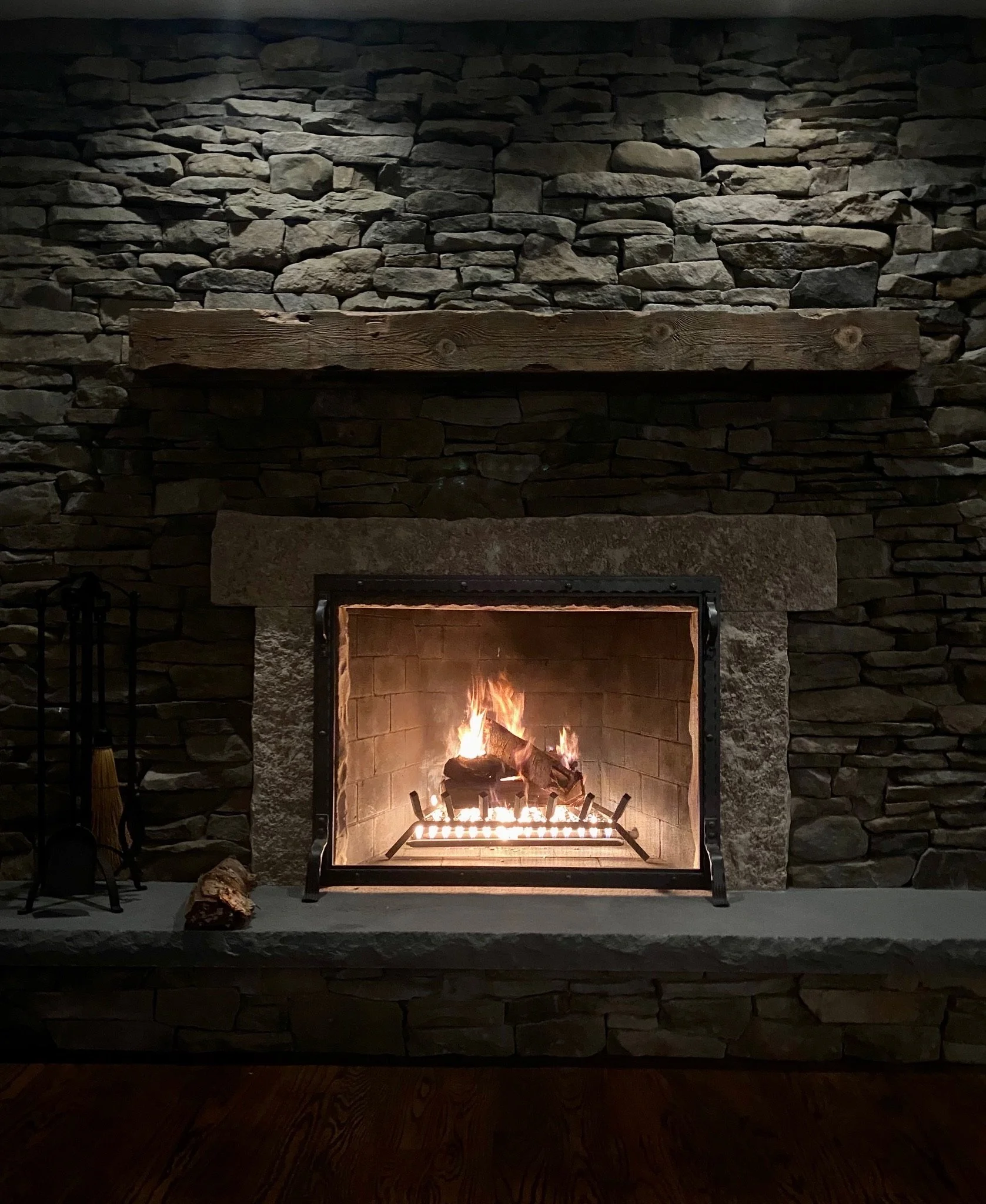 Fireplace with a stone and wooden mantle, lit with a fire at the bottom, surrounded by a dark interior.