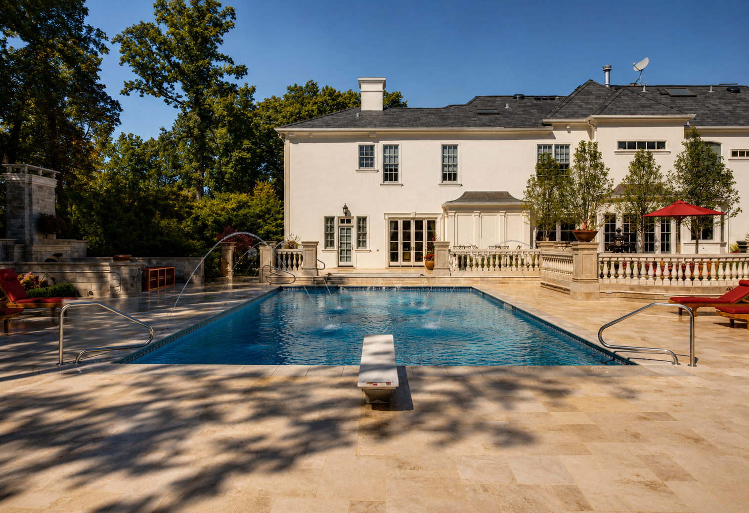 A luxurious backyard with a large swimming pool, surrounded by a stone deck and patio furniture, with a white two-story house and lush green trees in the background.