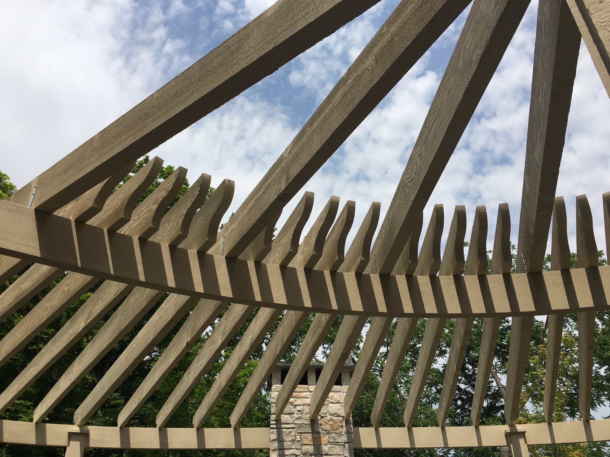 Wooden fence with vertical slats, stone pillar, blue sky with clouds, and greenery visible in the background.