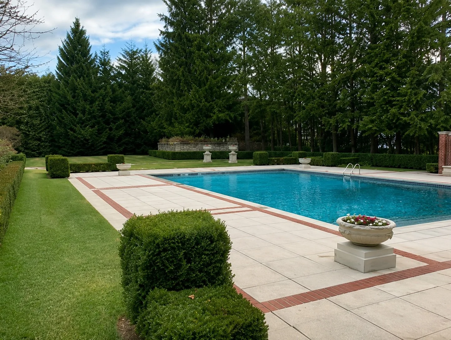 A backyard with a swimming pool surrounded by well-manicured grass, hedges, and trees.