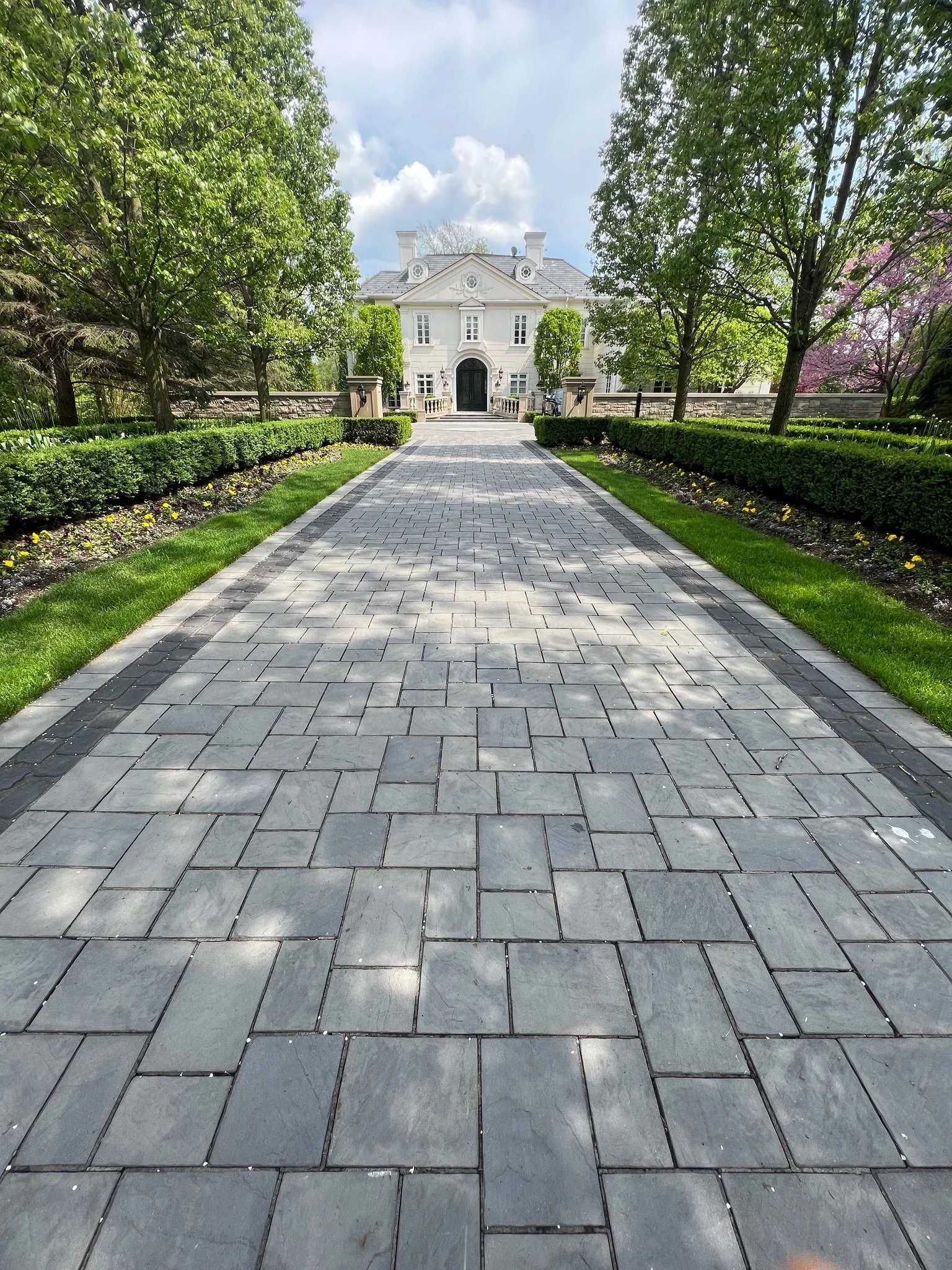 Paved pathway leading to a large white house with trees on both sides.