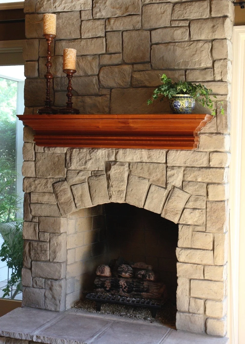 Stone fireplace with a wooden mantel, decorated with two candles on candlesticks and a potted plant in a blue and white ceramic pot.
