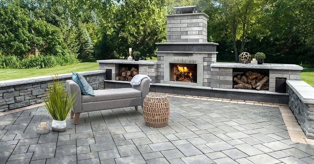 Outdoor patio with a stone fireplace, a gray bench, decorative objects, and surrounding greenery