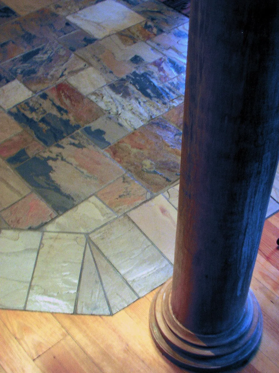 Close-up of colorful stone tile flooring next to a dark wooden pillar.