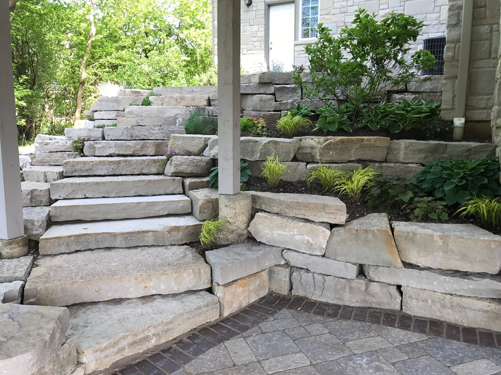 Stone stairs leading to a house entrance, with green bushes and trees in the background.