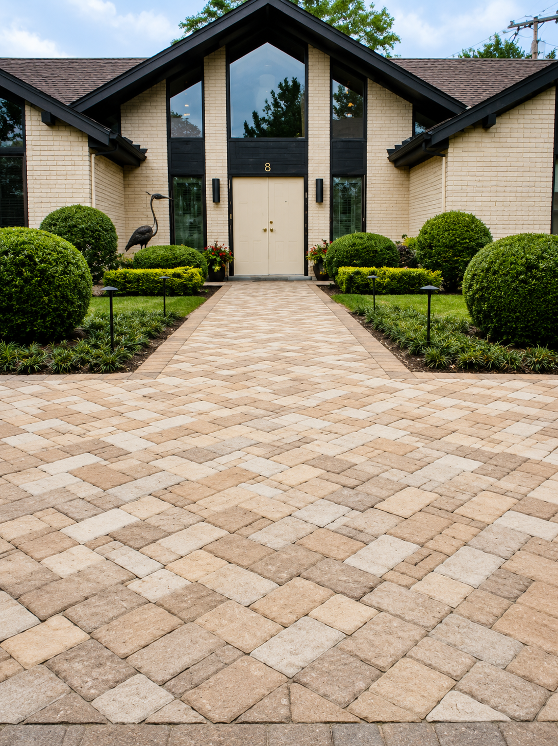 Front view of a modern house with a brick exterior, large front door, symmetrical landscaping, and a brick walkway leading to the entrance.