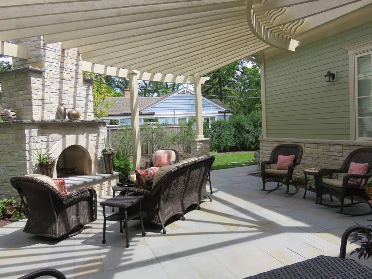 Backyard patio with wicker furniture, outdoor fireplace, and a green house wall.