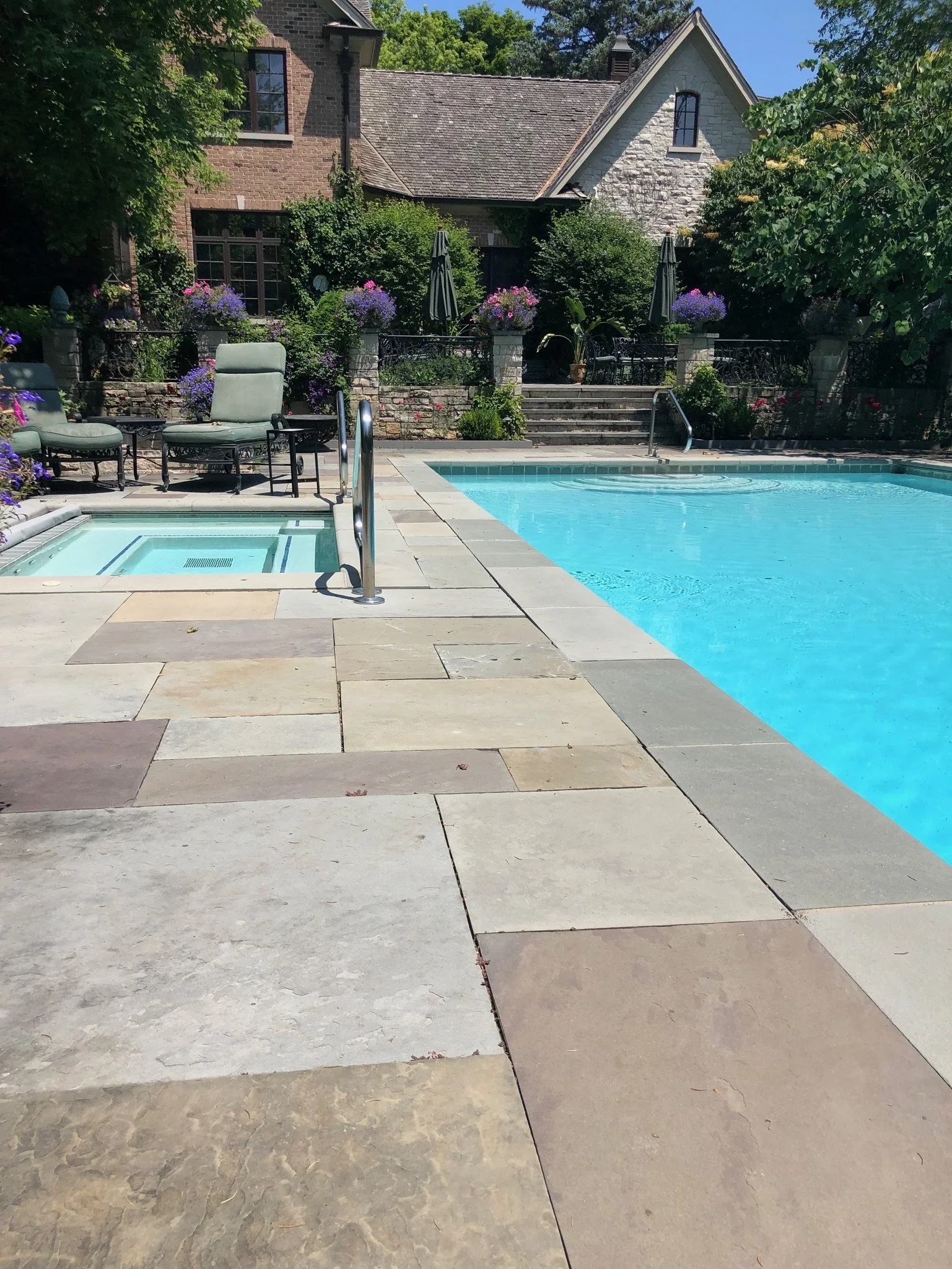 An outdoor backyard with a swimming pool, patio furniture, lush greenery, and a house in the background.