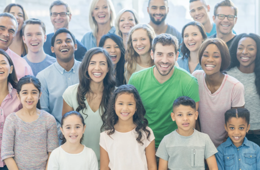 Group of diverse smiling adults and children posing together indoors.