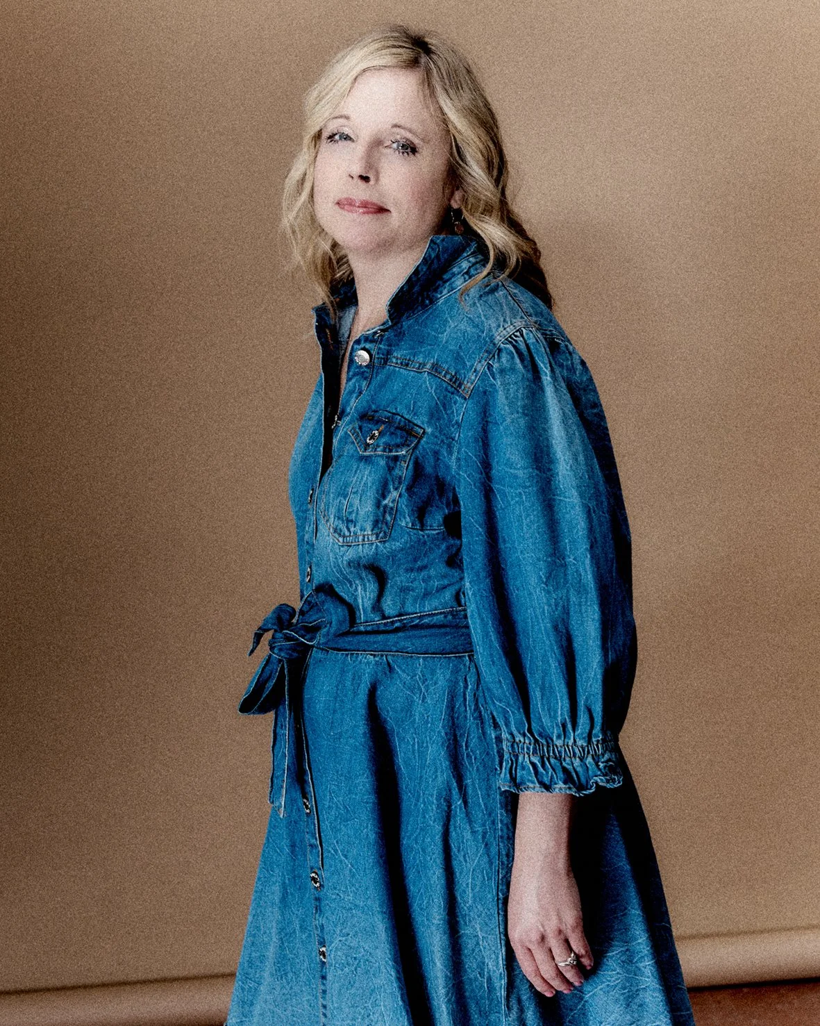  A series of portraits of Georgie. She has shoulder length blonde, wavy hair and is shown from the chest up, turned slightly to the side. She is wearing a denim jumpsuit and is smiling at the camera. 