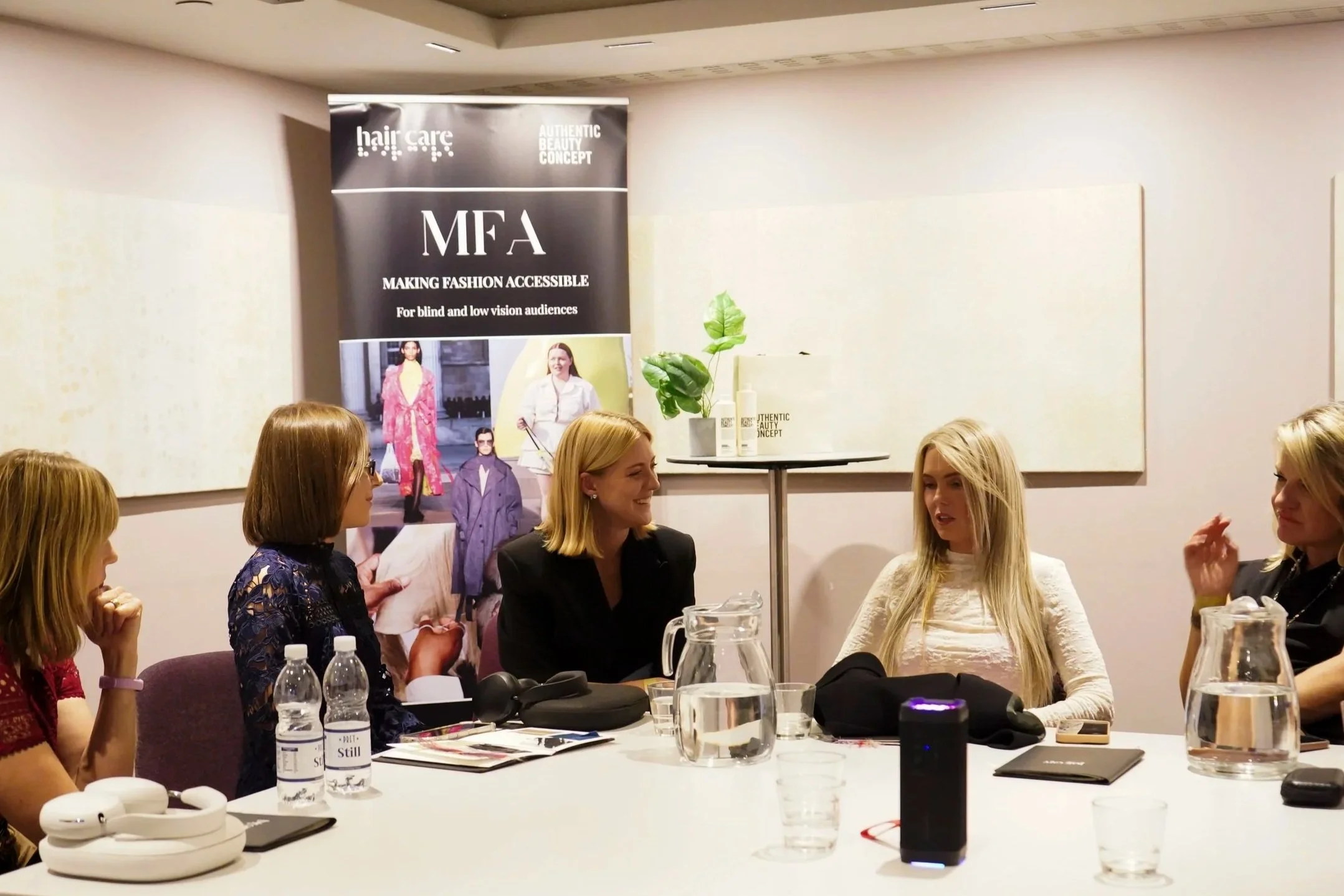 Five women chat around a table in front of a Making Fashion Accessible banner by Hair & Care and sponsored by Authentic Beauty Concept.