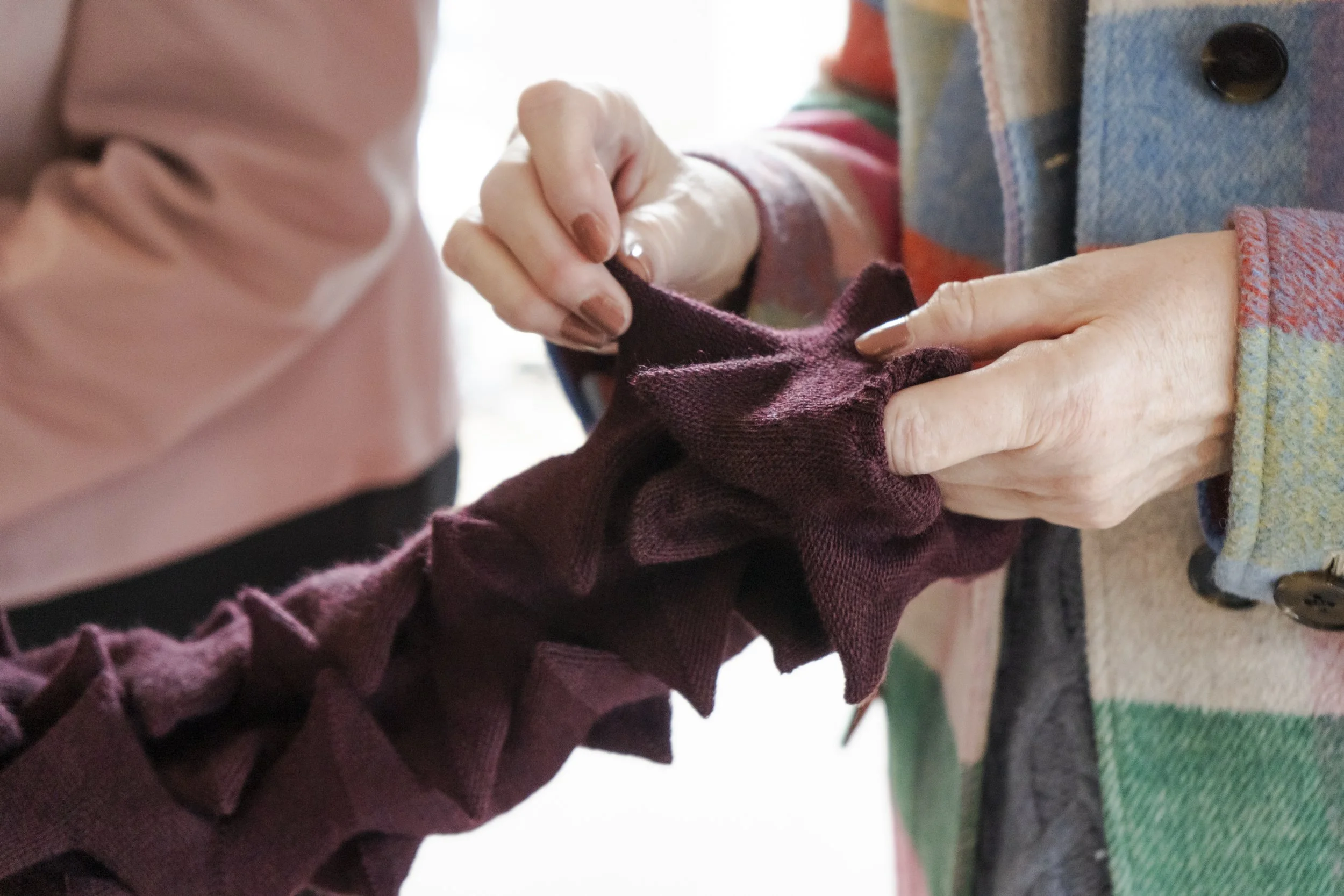 Close-up of a person's hands feeling a spiky knitted garment in a burgundy colour.