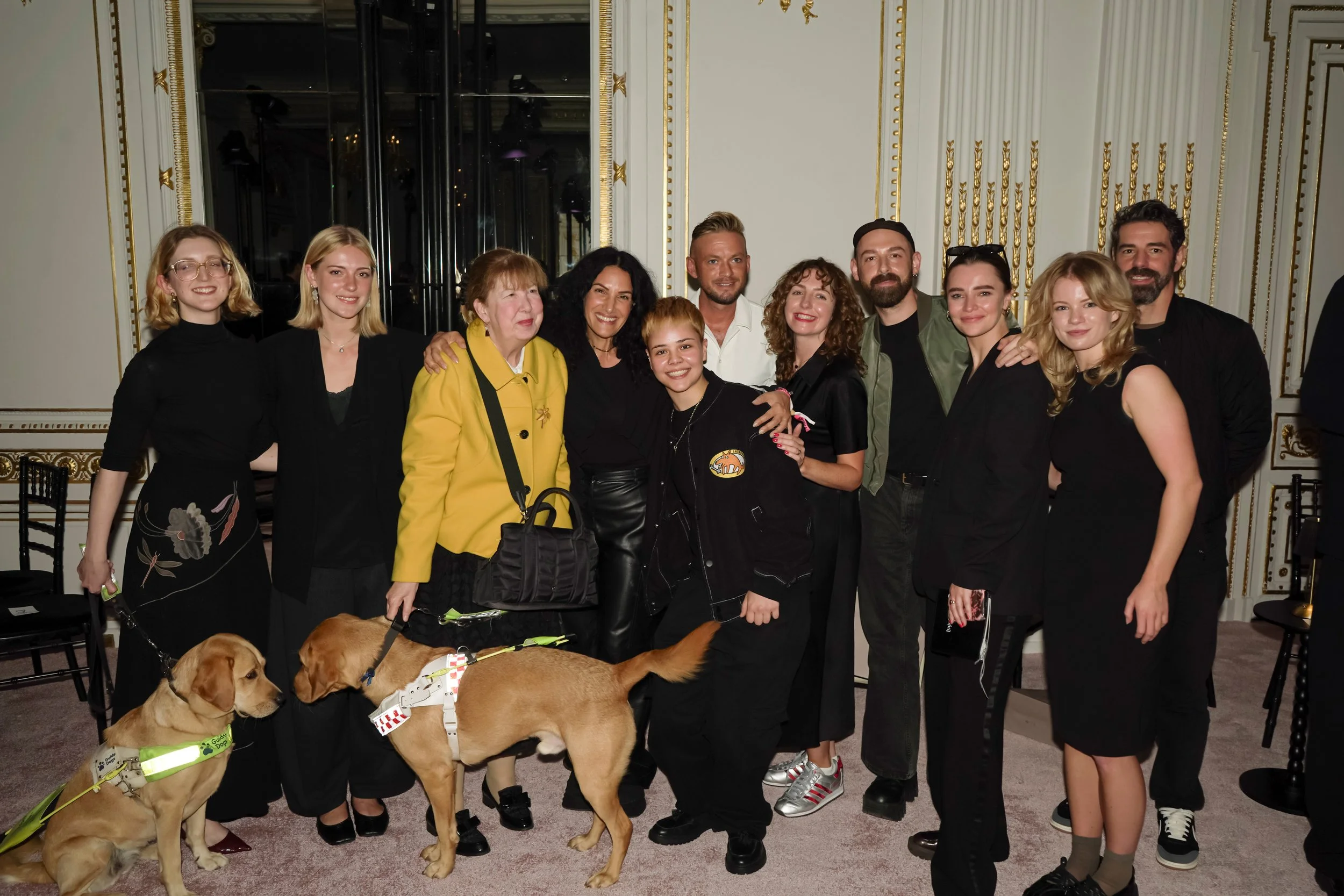 A group of guests pose together in an ornate white-and-gold room with two guide dogs.