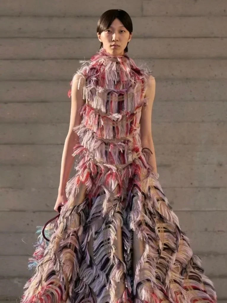 A model on the catwalk in a floor-length gown covered in layers of pink, red and lilac fringe.