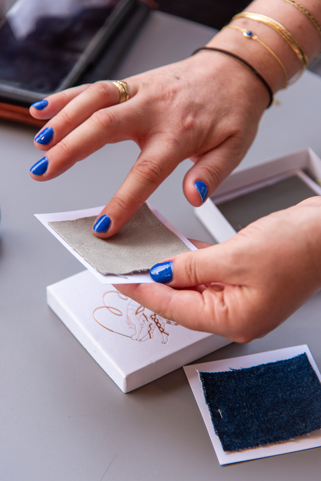 Close up of a person's hands as they feel the texture of a fabric sample; a pile of them arrange below.
