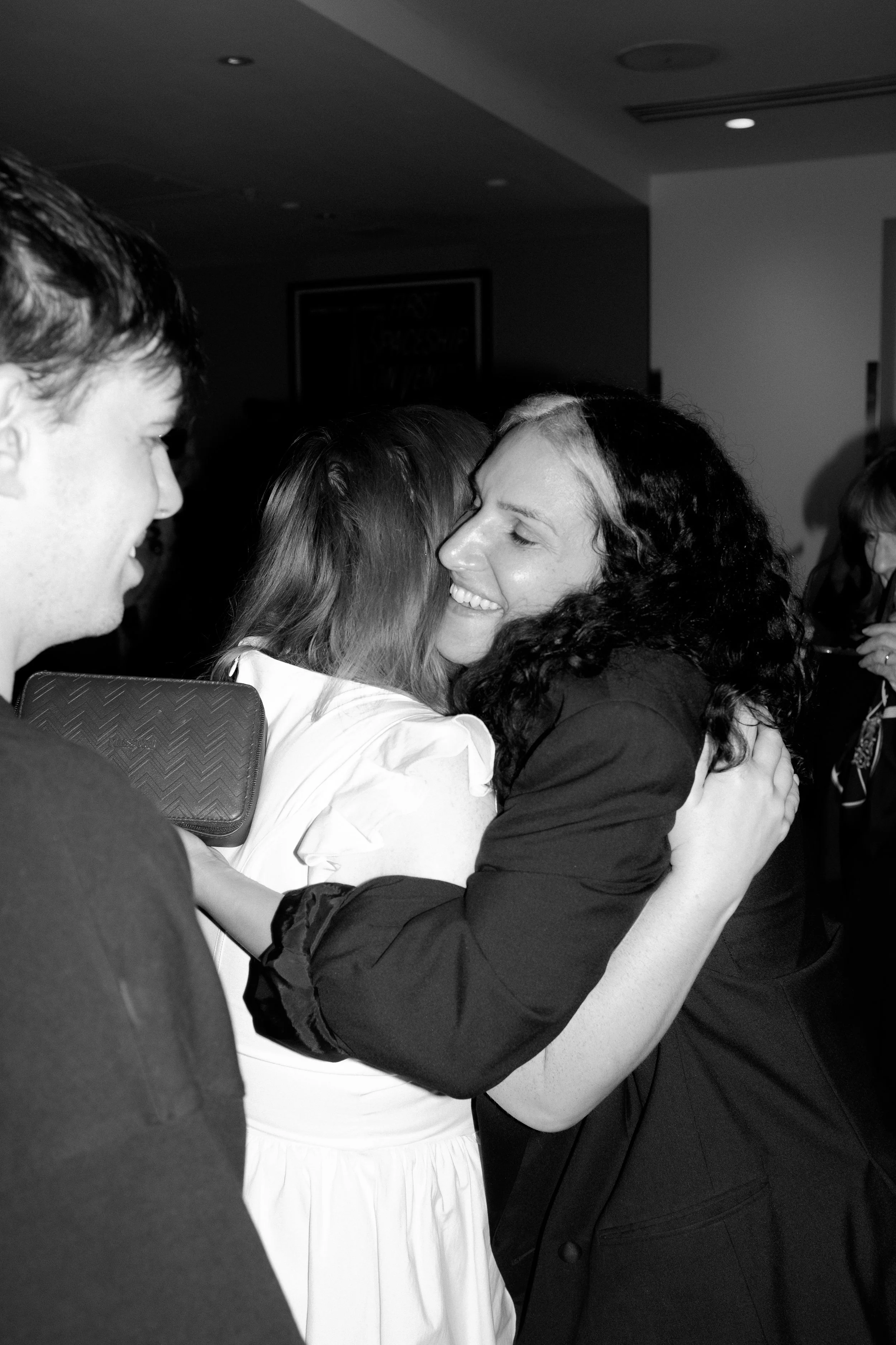 A woman smiling and hugging another person in a crowd at a busy event with people standing in the background