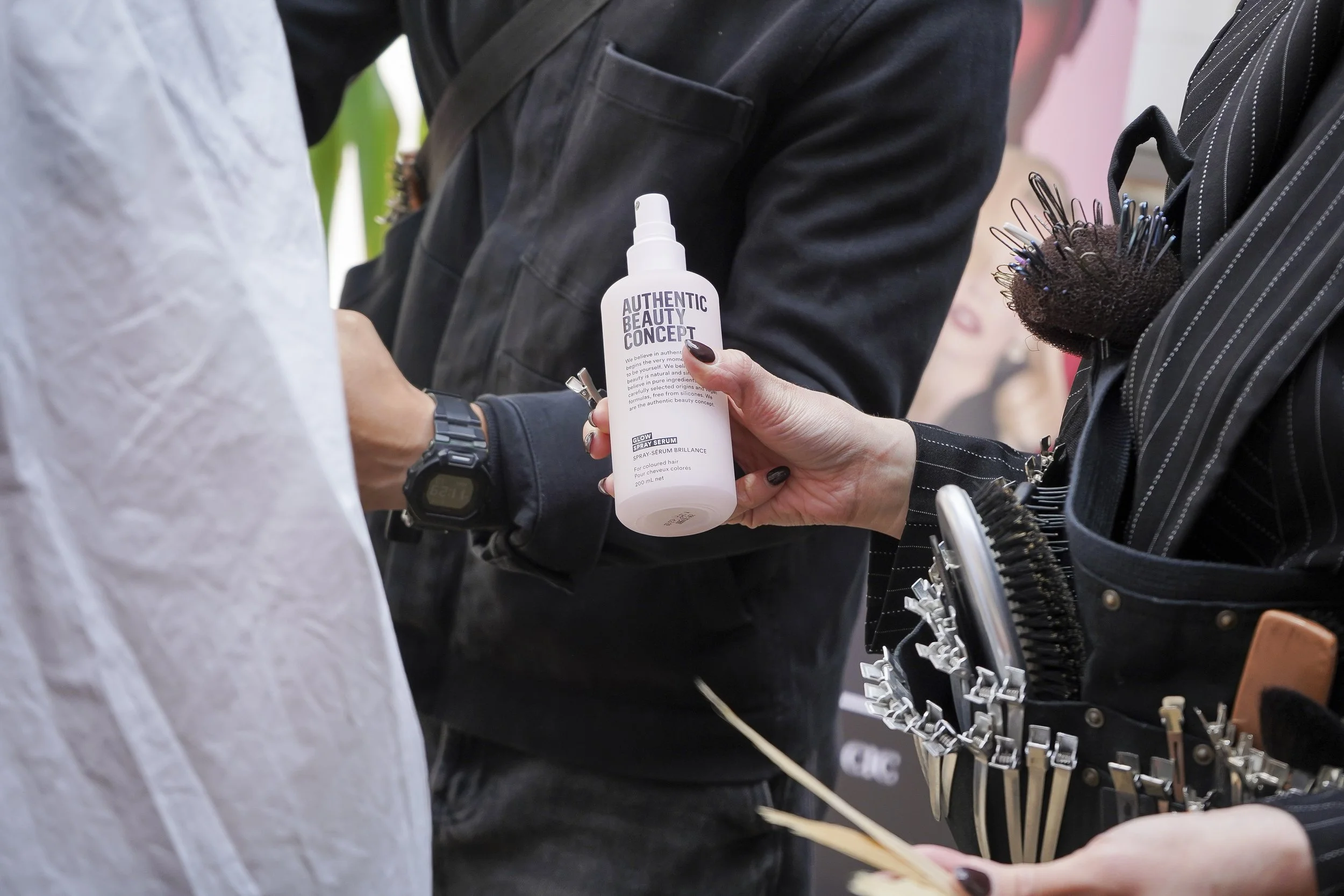 A person holding a white spray bottle labeled 'Authentic Beauty Concept' during a hairstyling event
