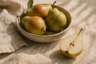 A bowl of fresh pears next to a halved pear on a wrinkled cloth.