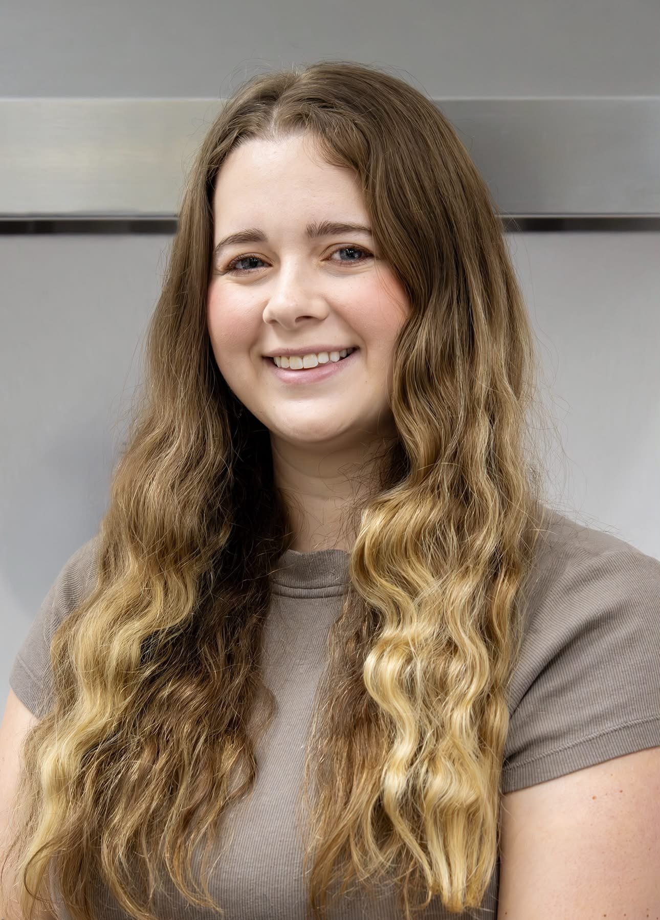 A young woman with long, wavy, light brown hair smiling at the camera.