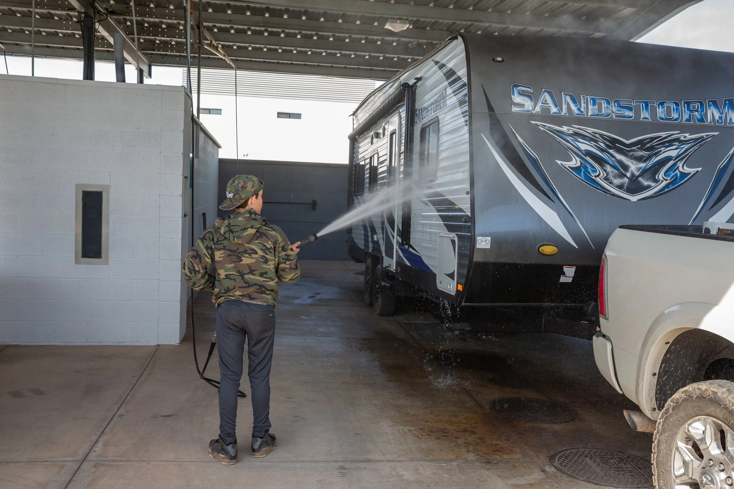 Customer power-washing a travel trailer at the free self-service RV wash bay at Carefree Covered RV Storage near I-10 in Chandler, AZ