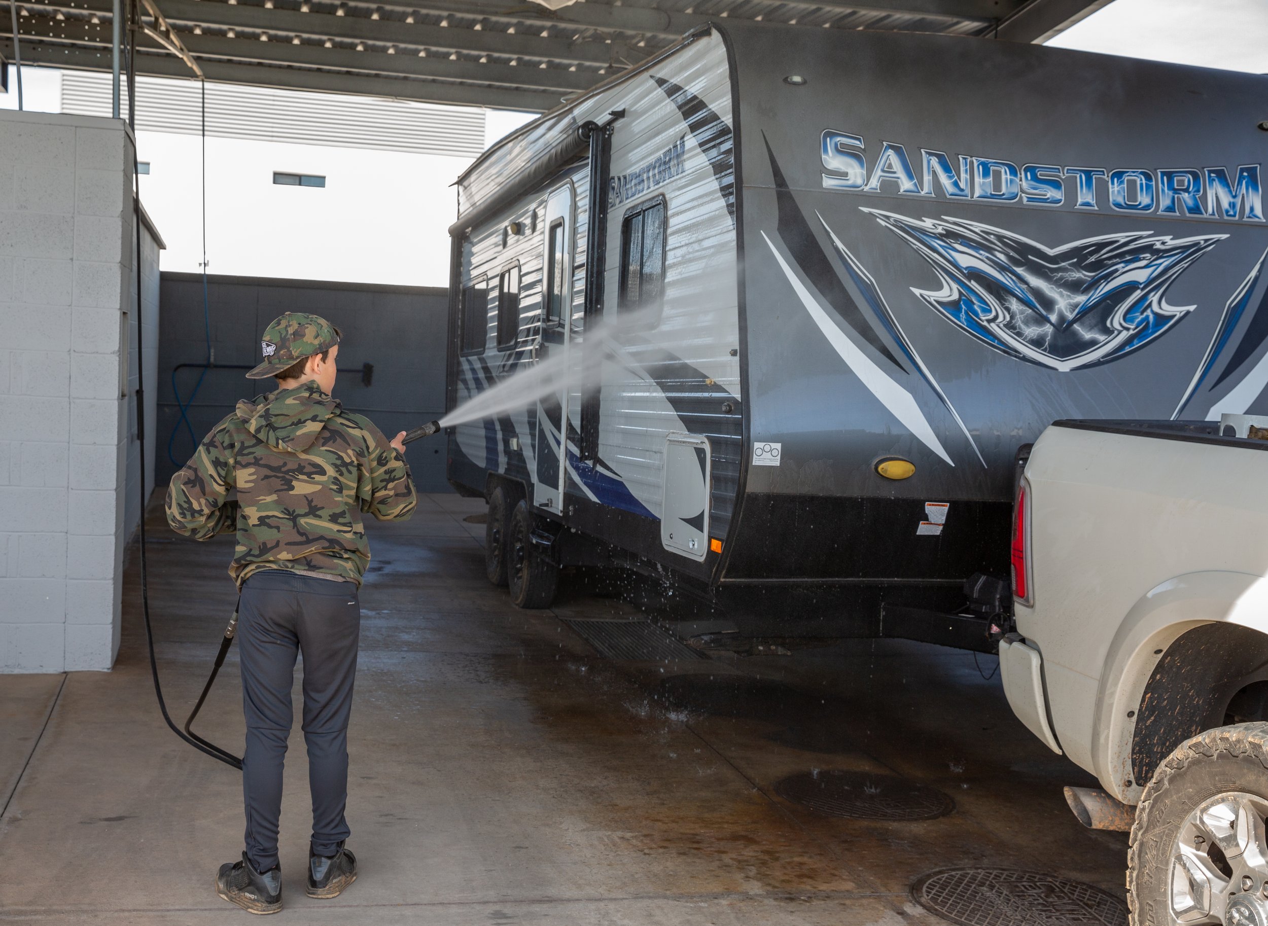 Customer power-washing a travel trailer at the free self-service RV wash bay at Carefree Covered RV Storage's Chandler Kyrene Rd location