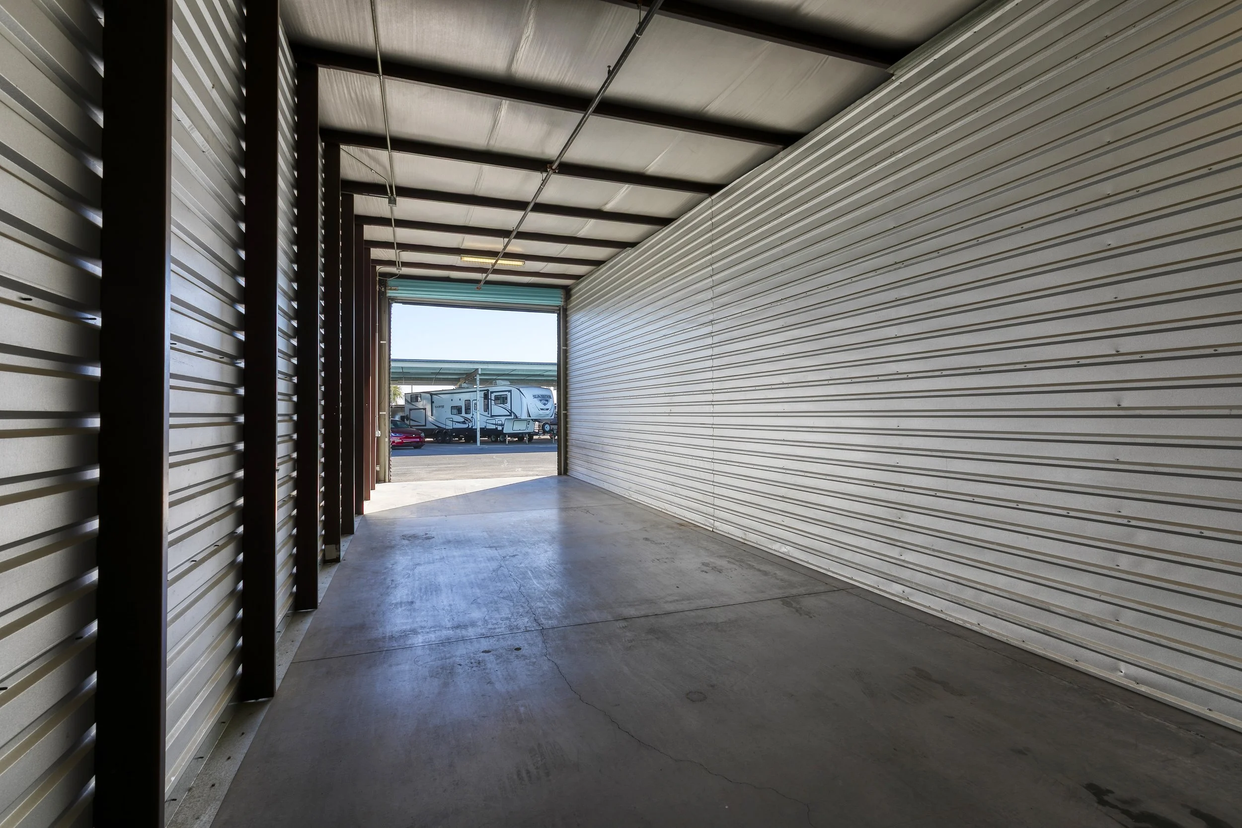 Interior view of an open enclosed RV garage unit looking out toward a parked travel trailer in Chandler, AZ
