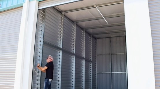 Facility staff member opening a roll-up door to reveal an empty, well-lit enclosed RV storage unit at Wylie Bargain Storage