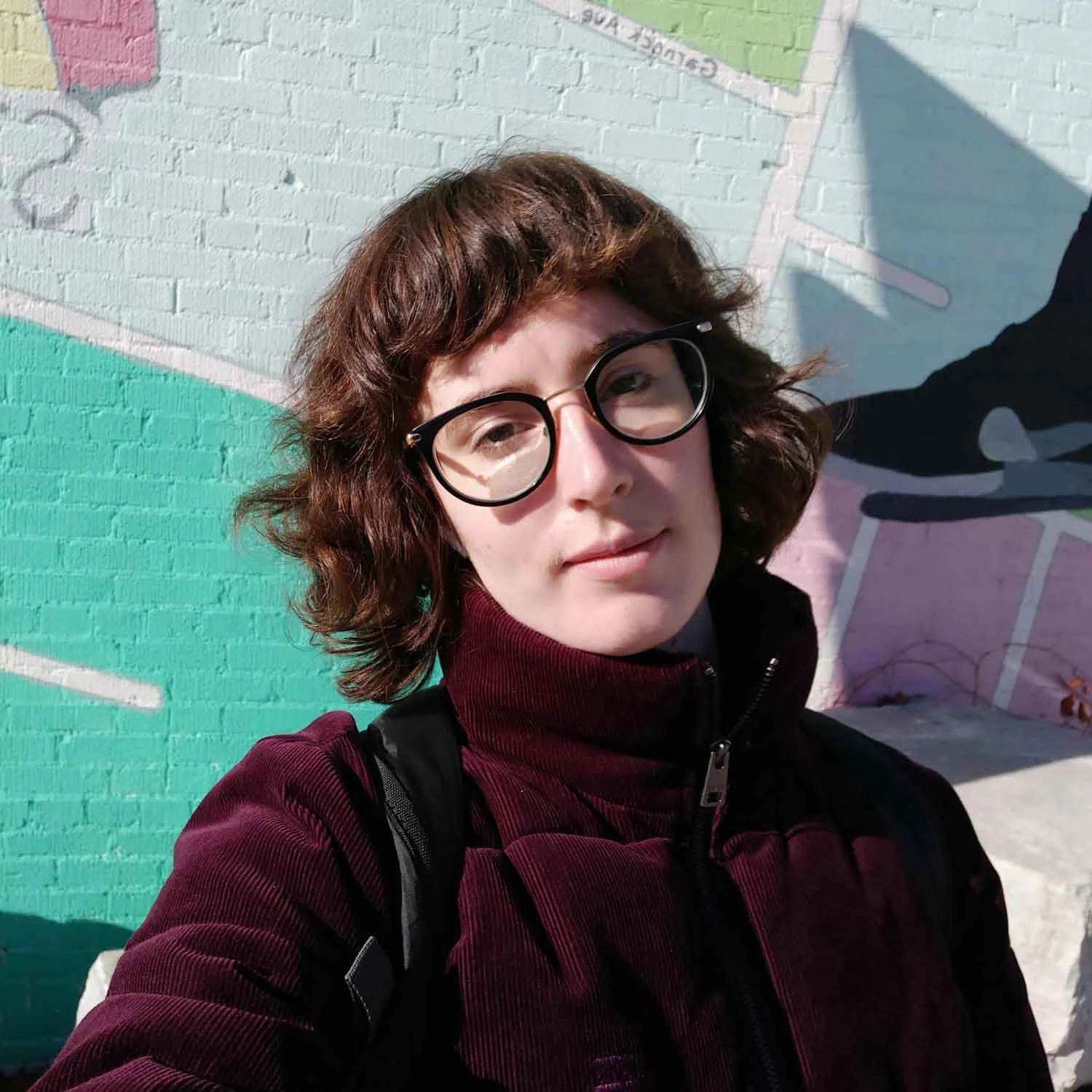 A headshot of Mairéad standing in front of a colourful wall