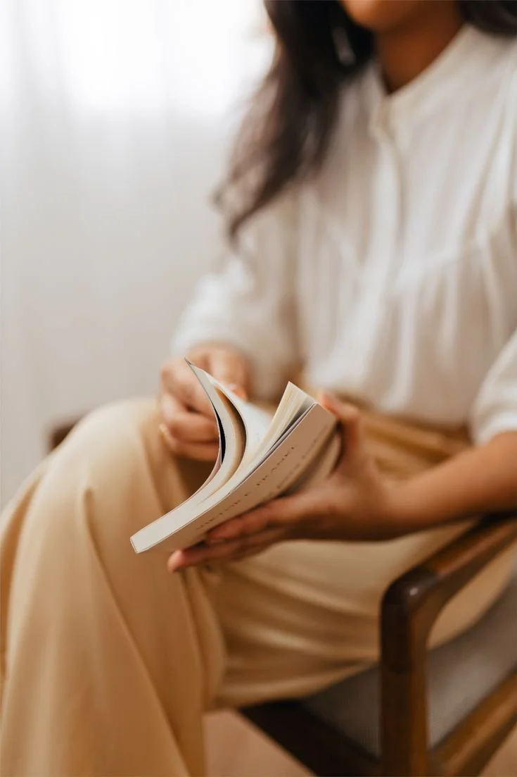 Person sitting comfortably and reading a book in a calm, softly lit setting.