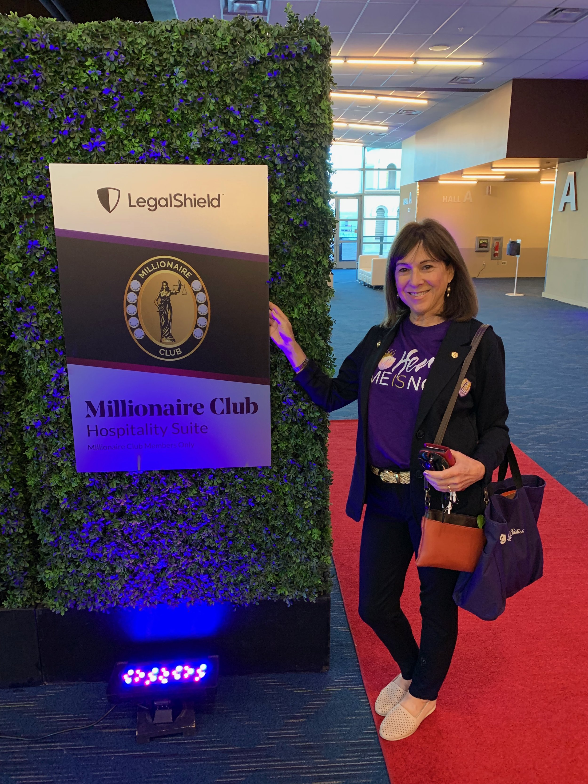 Nancy Chaconas stands in front of a large sign, celebratingin the LegalShield Millionaire Club
