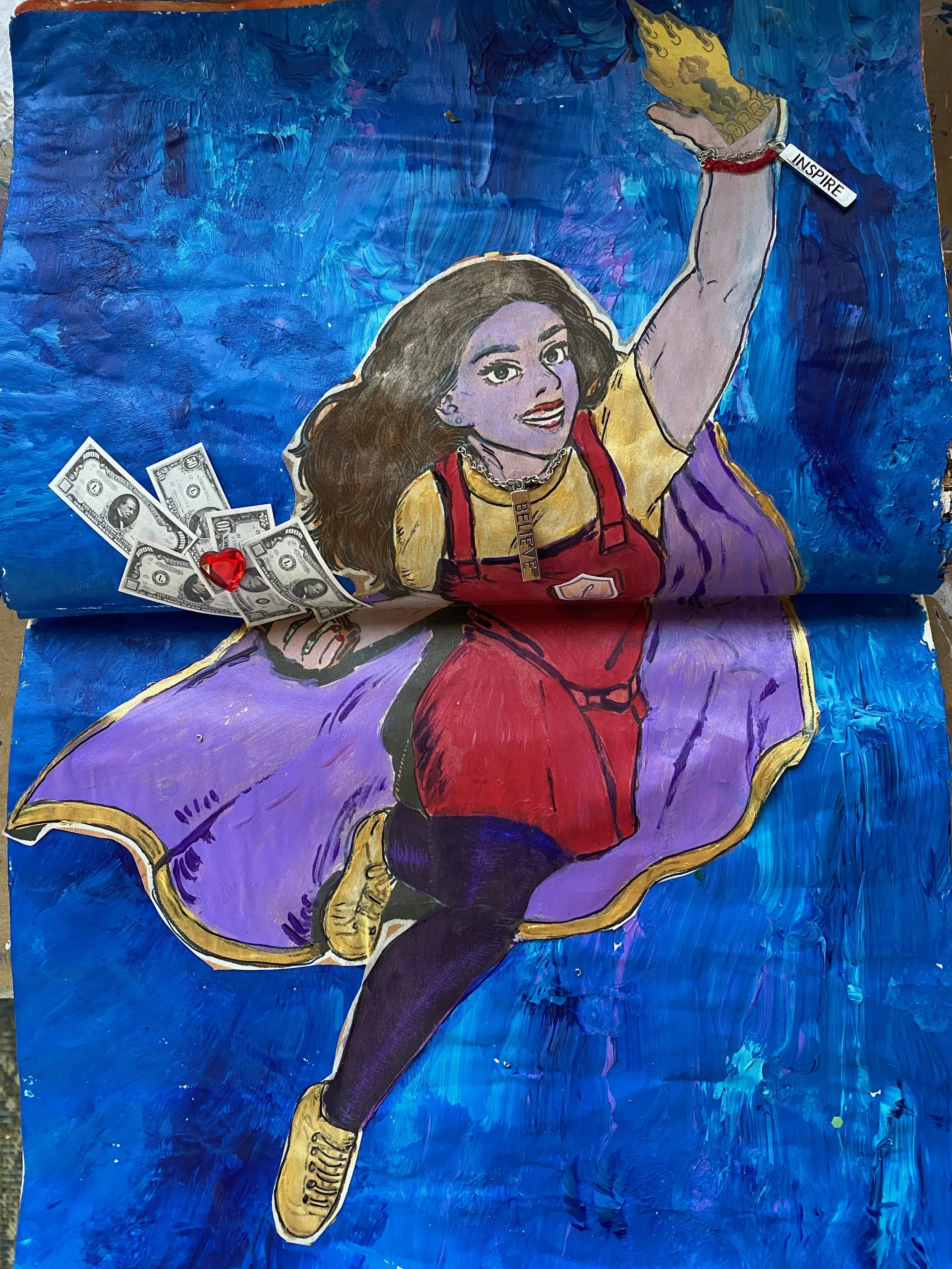 A mixed media artwork featuring a cartoon of a woman with long dark hair, wearing yellow and red with a chain necklace that spells 'BELIEVE'. The woman is reaching upward with her right arm, holding a tag that says 'INSPIRE'. There is a collage eleme