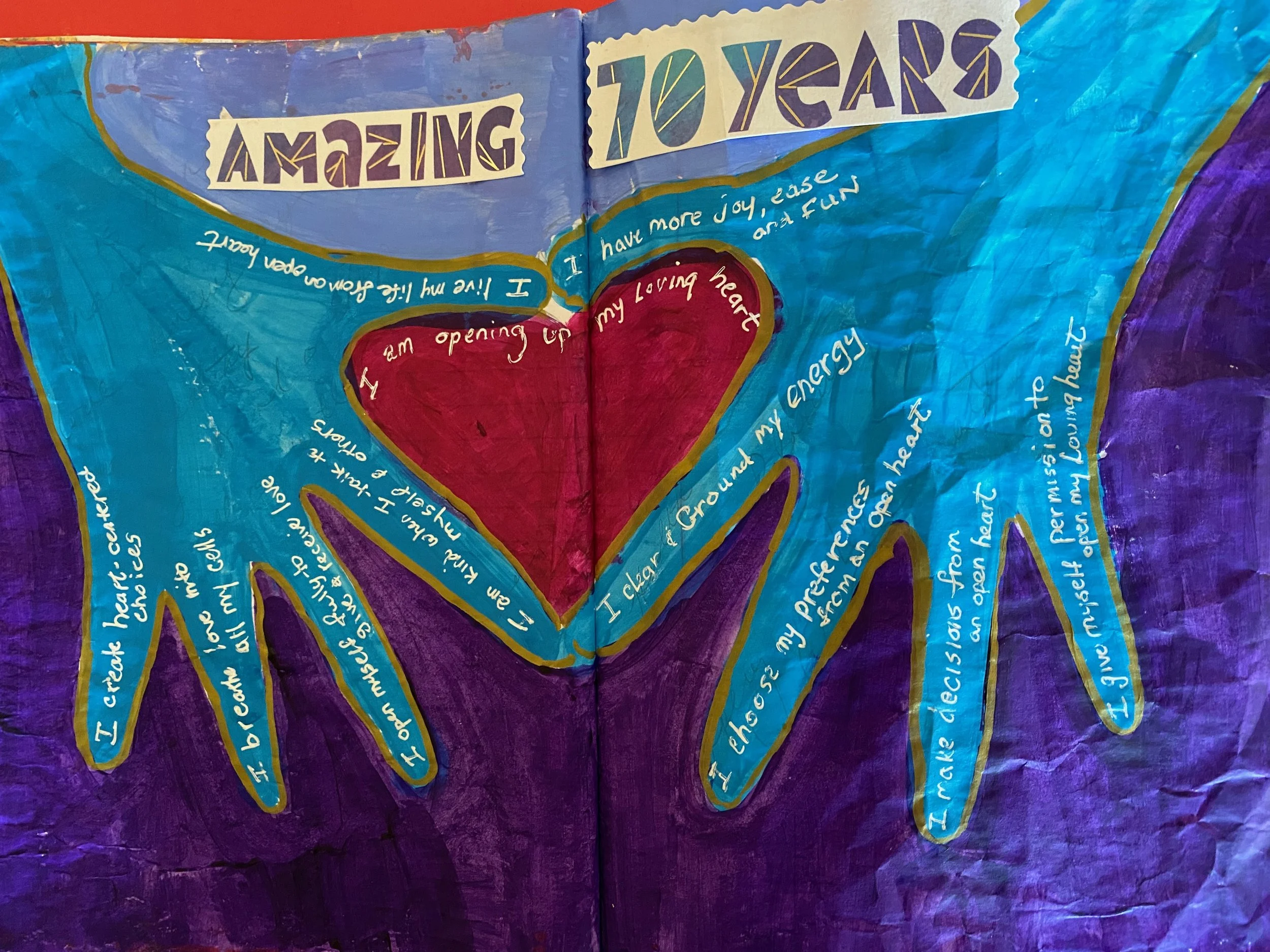 A handmade poster with colorful, painted background and a large red heart in the center, surrounded by handwritten messages in white ink.
