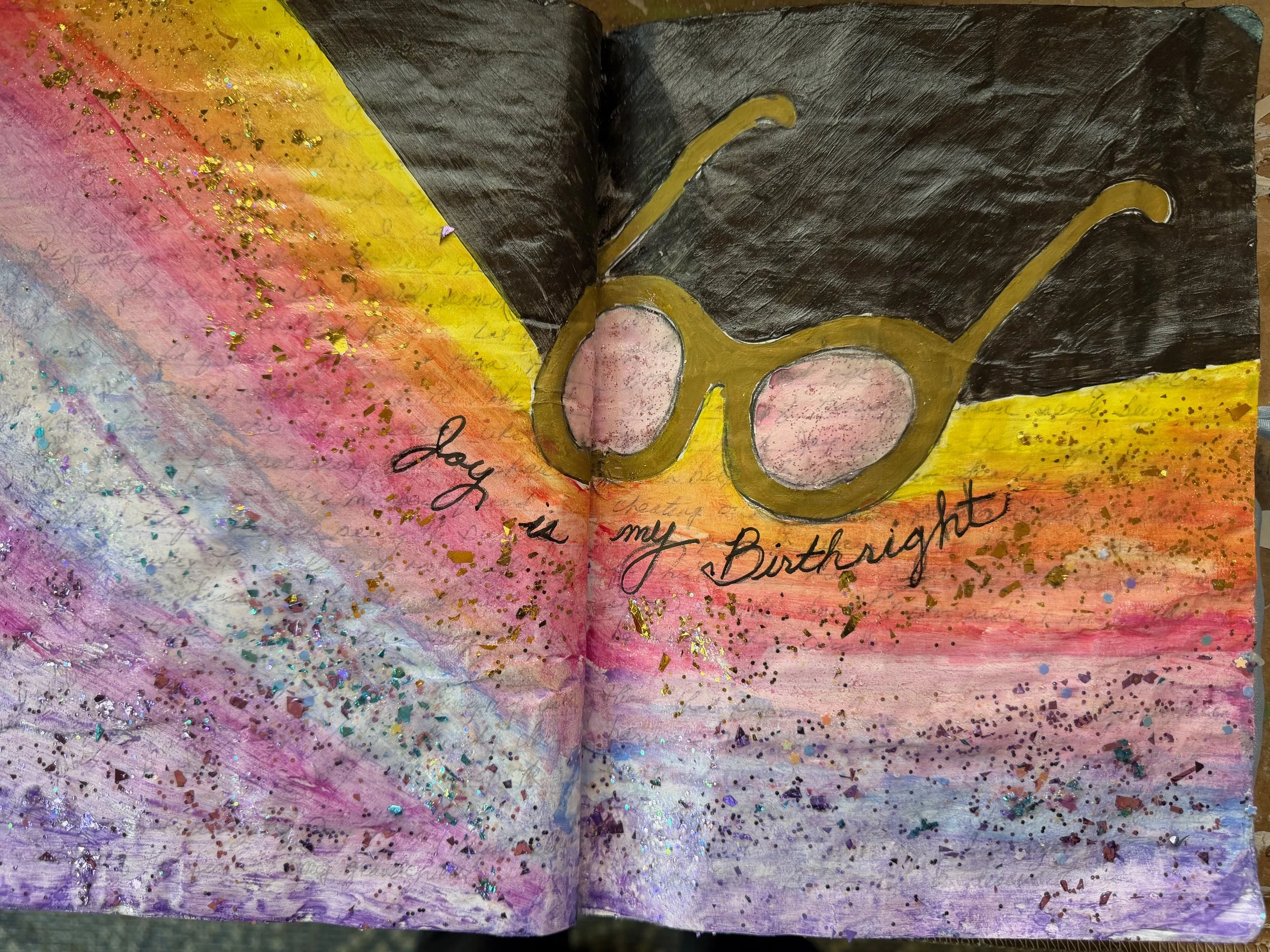 A colorful artwork with a black background, yellow and pink hues, and gold glitter accents. It features a pair of glasses and handwritten text, including the words 'joy' and 'birthday'.