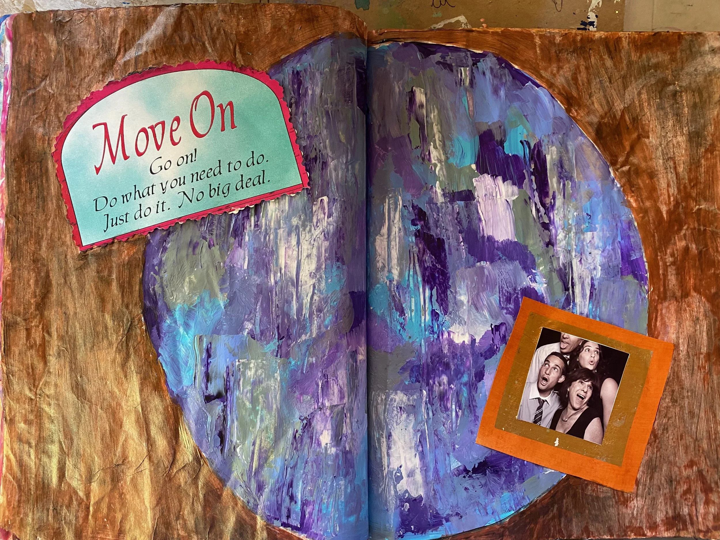 An open book with an illustrated waterfall and a small photograph of four people smiling and making funny faces, with a colorful border, placed on a wooden surface.