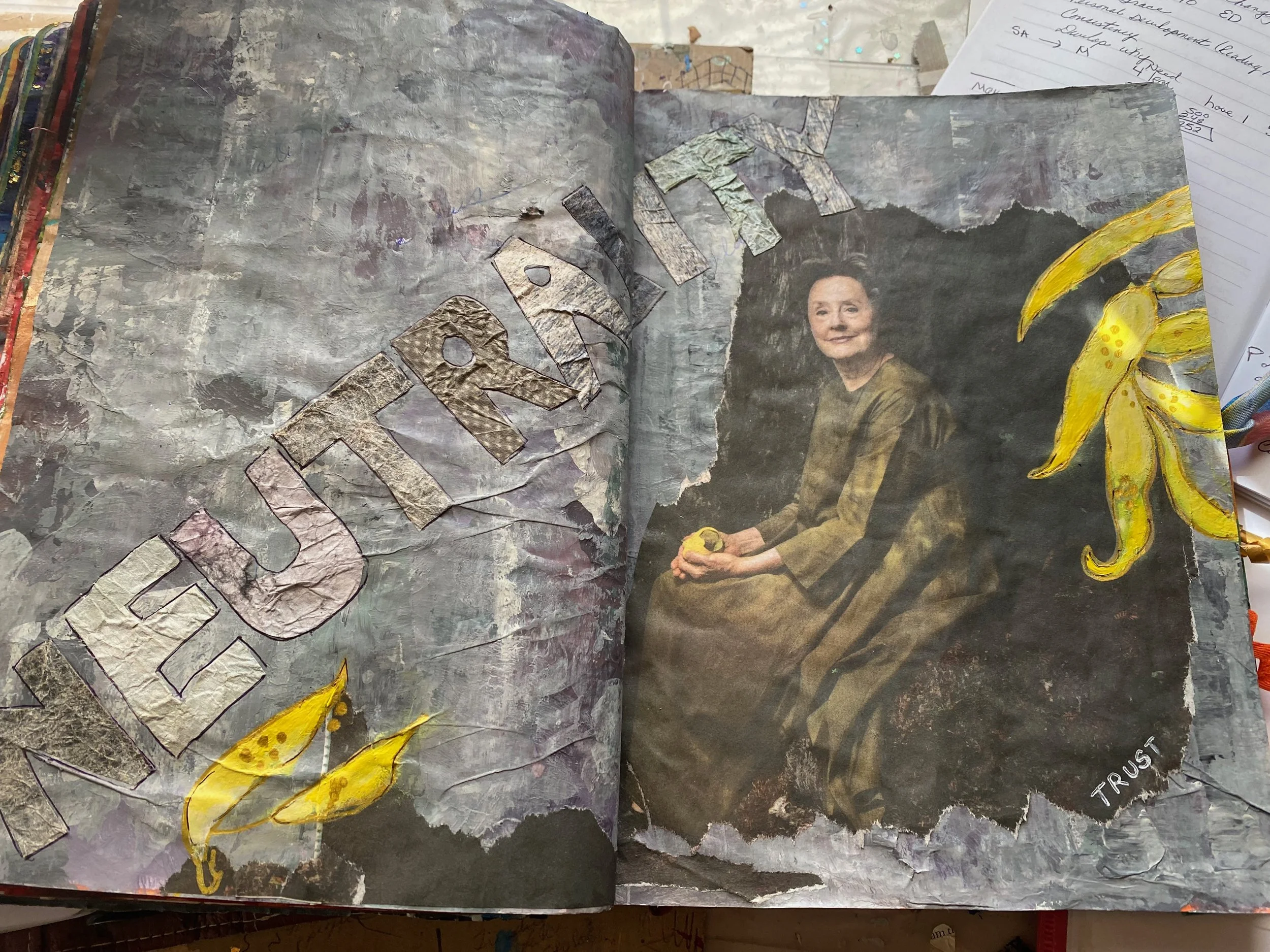 A scrapbook or art journal with torn paper, collage elements, a painted yellow banana, and a photograph of a woman holding something. The background has a textured, muted gray and purple tone with handwritten notes and papers nearby.