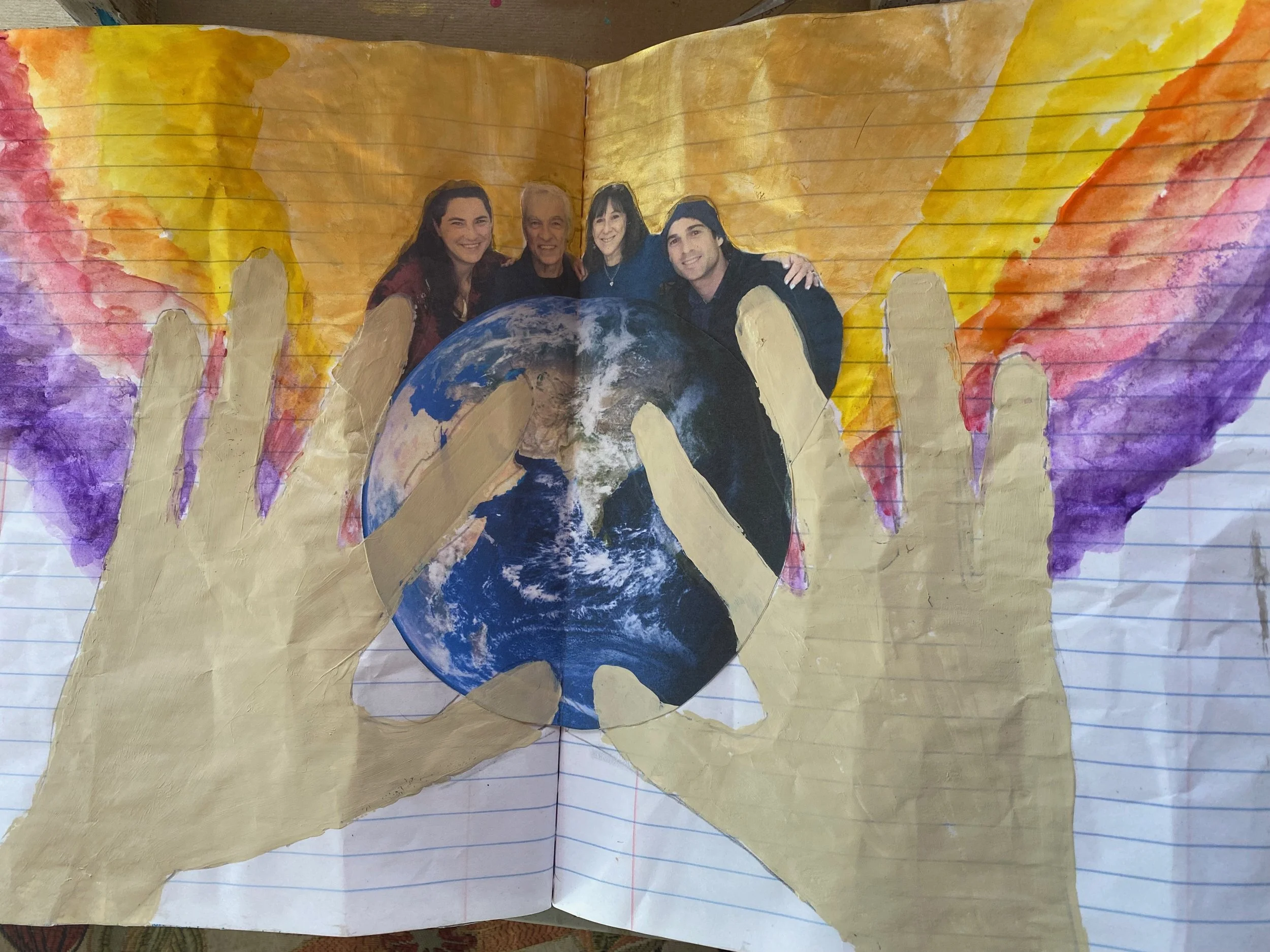A child’s drawing of the Earth with people holding hands on top, surrounded by colorful wings and a golden background, painted on lined notebook paper.